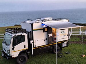 LuxLander 4.2m hard-top motorhome POD on an Isuzu NPS 300 4x4, parked by the sea with awning out