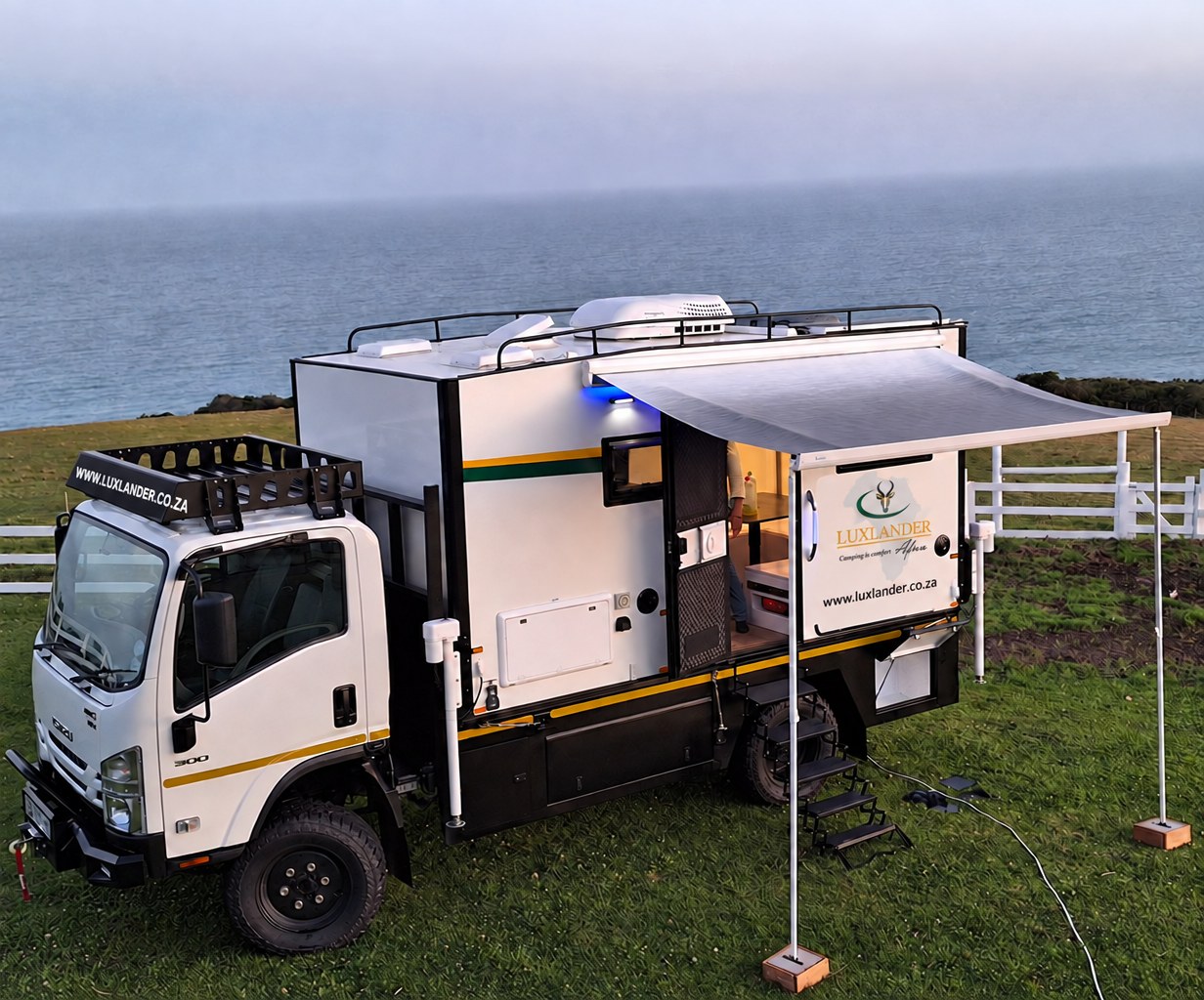 LuxLander 4.2m hard-top motorhome POD on an Isuzu NPS 300 4x4, parked by the sea with awning out